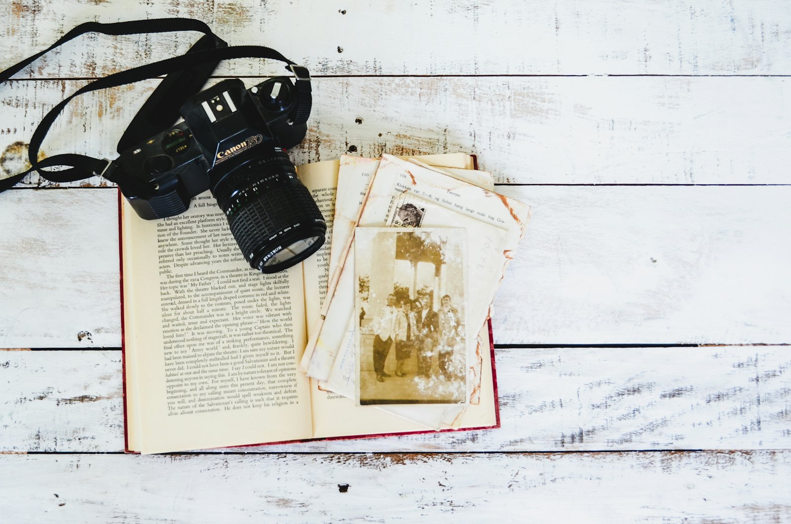 An old book, a camera and loose photographs on a table.